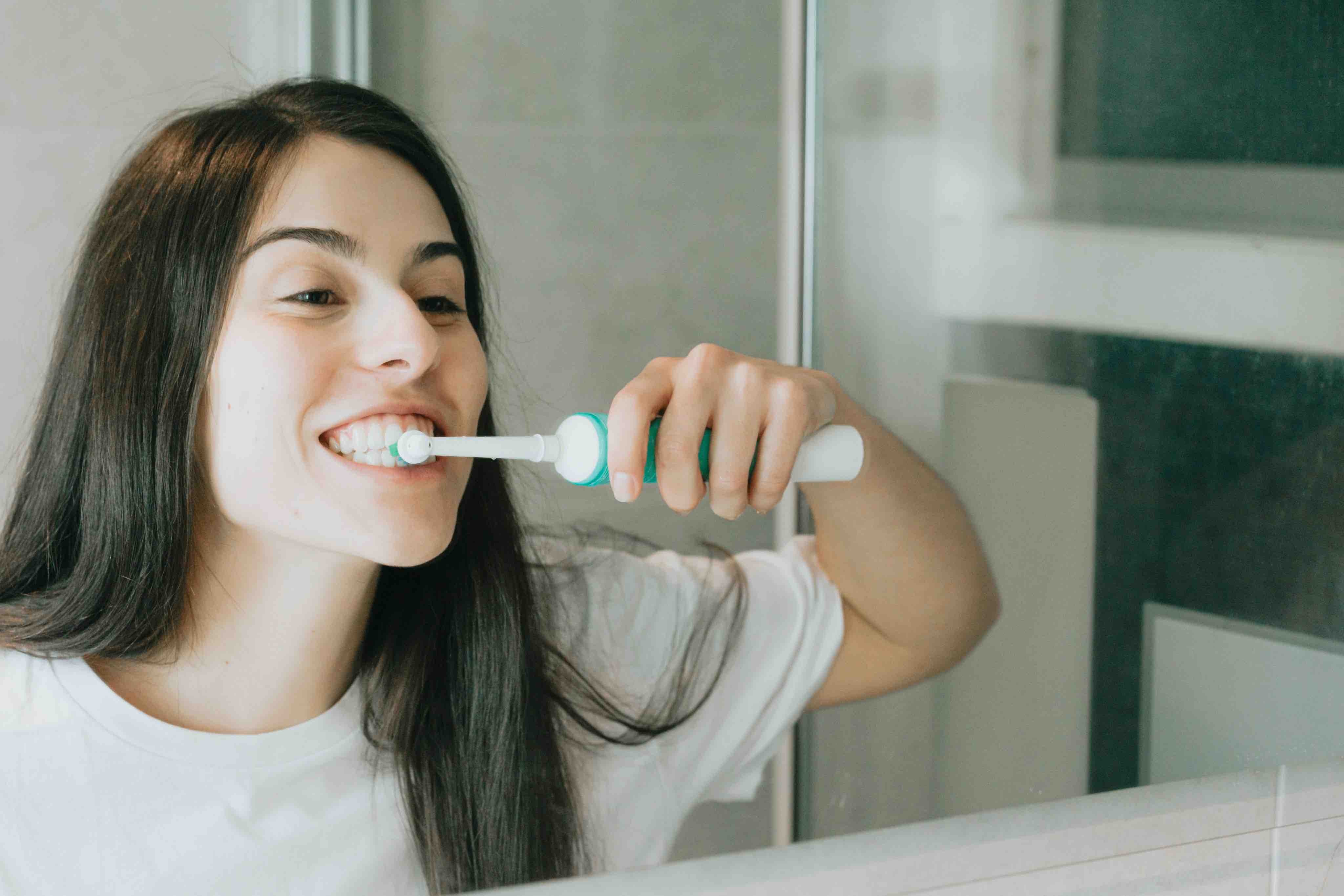 Une femme se brosse les dents avec une brosse à dents électrique dans un miroir